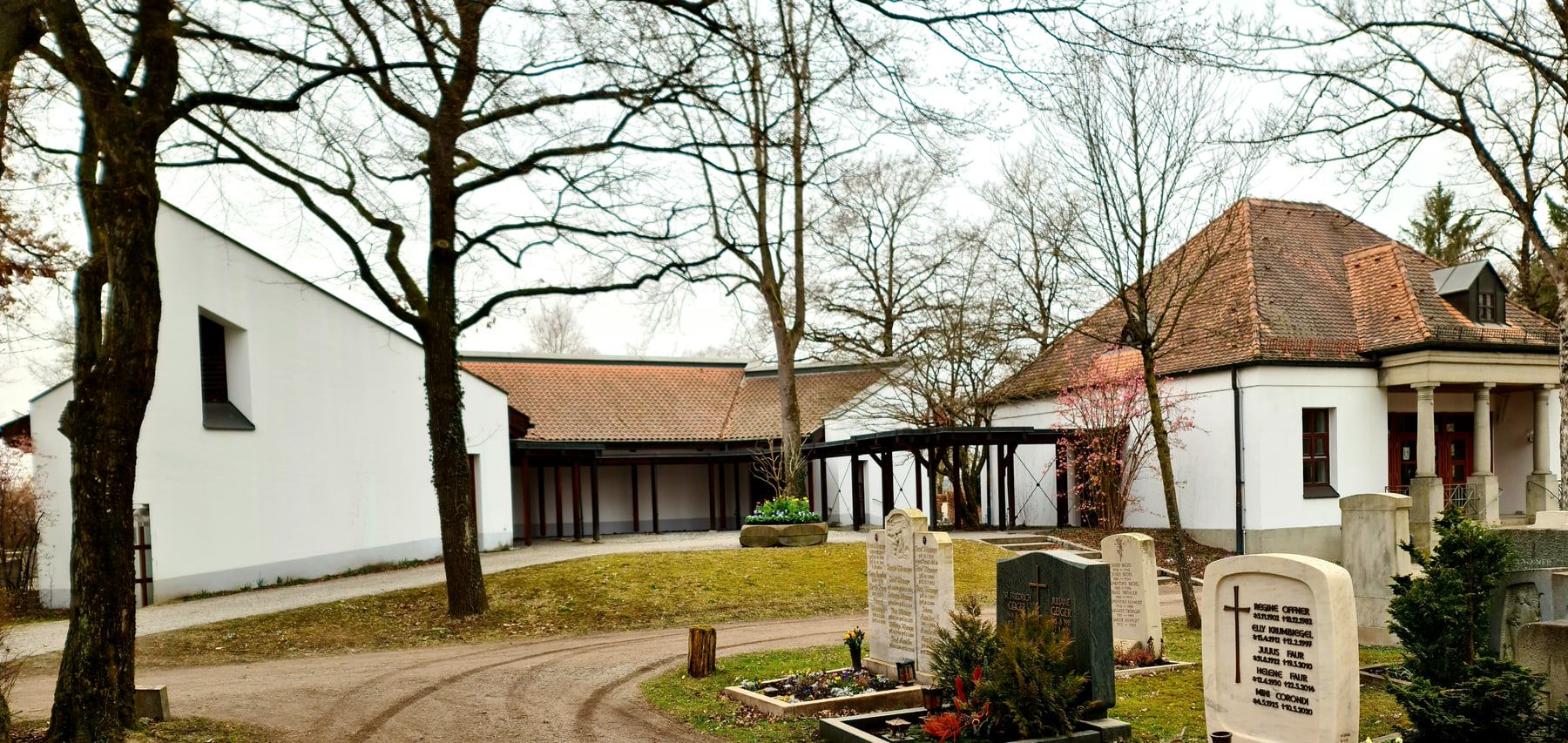 New and old funeral halls linked by a covered walkway behind a burial field at Aubing Cemetery